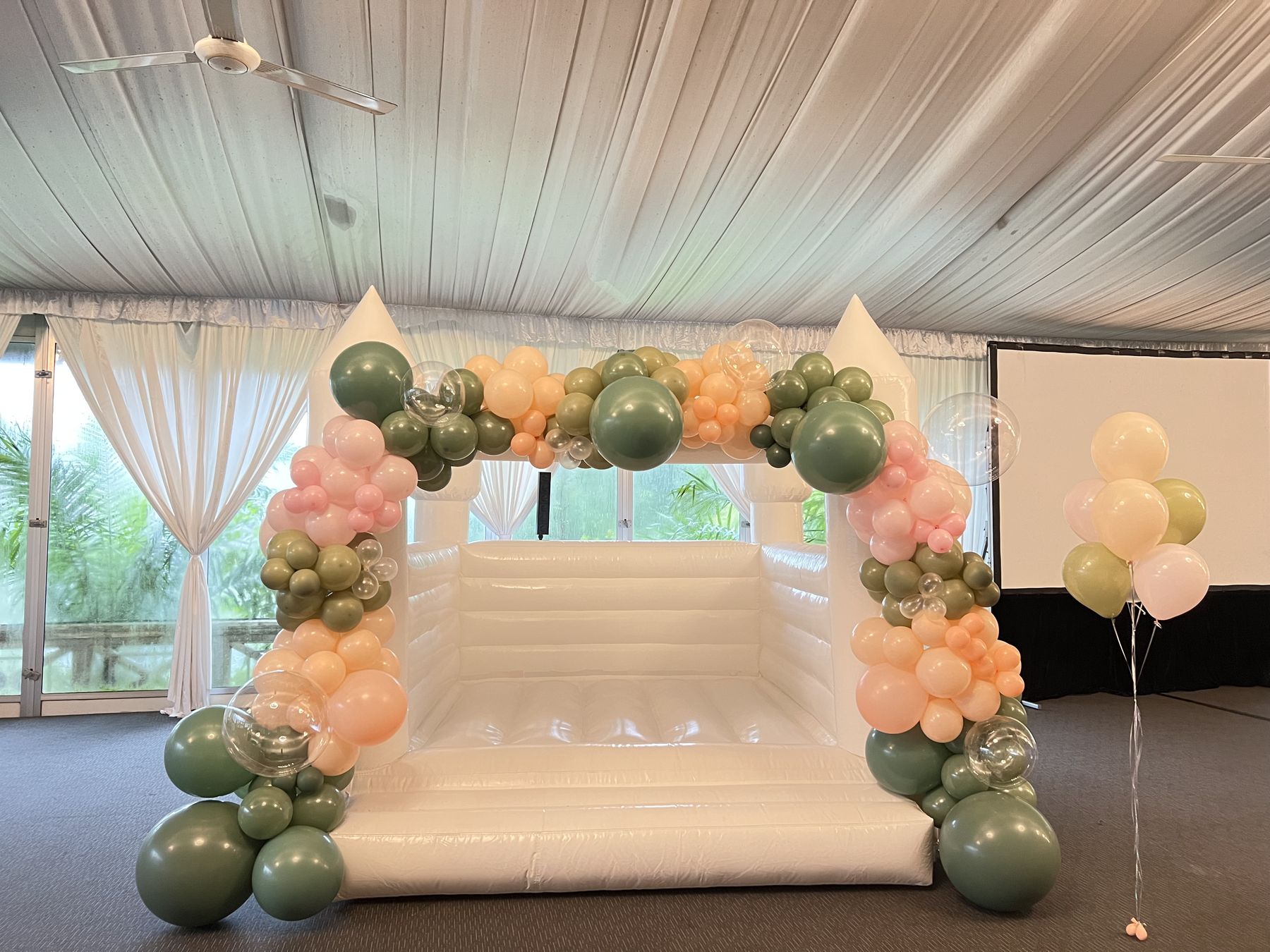 White bouncy castle with sage and peach balloons